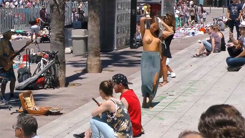 Pretty and joyful girl dances to the music and strips naked in the street