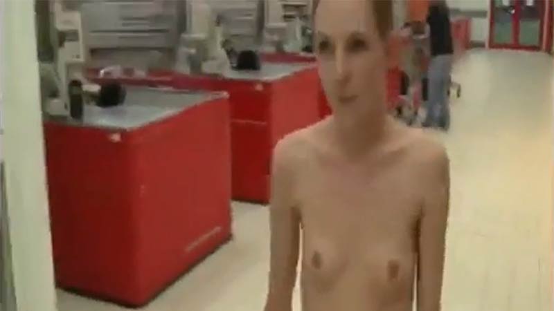 Waifish blonde girl walks around in a large supermarket completely naked
